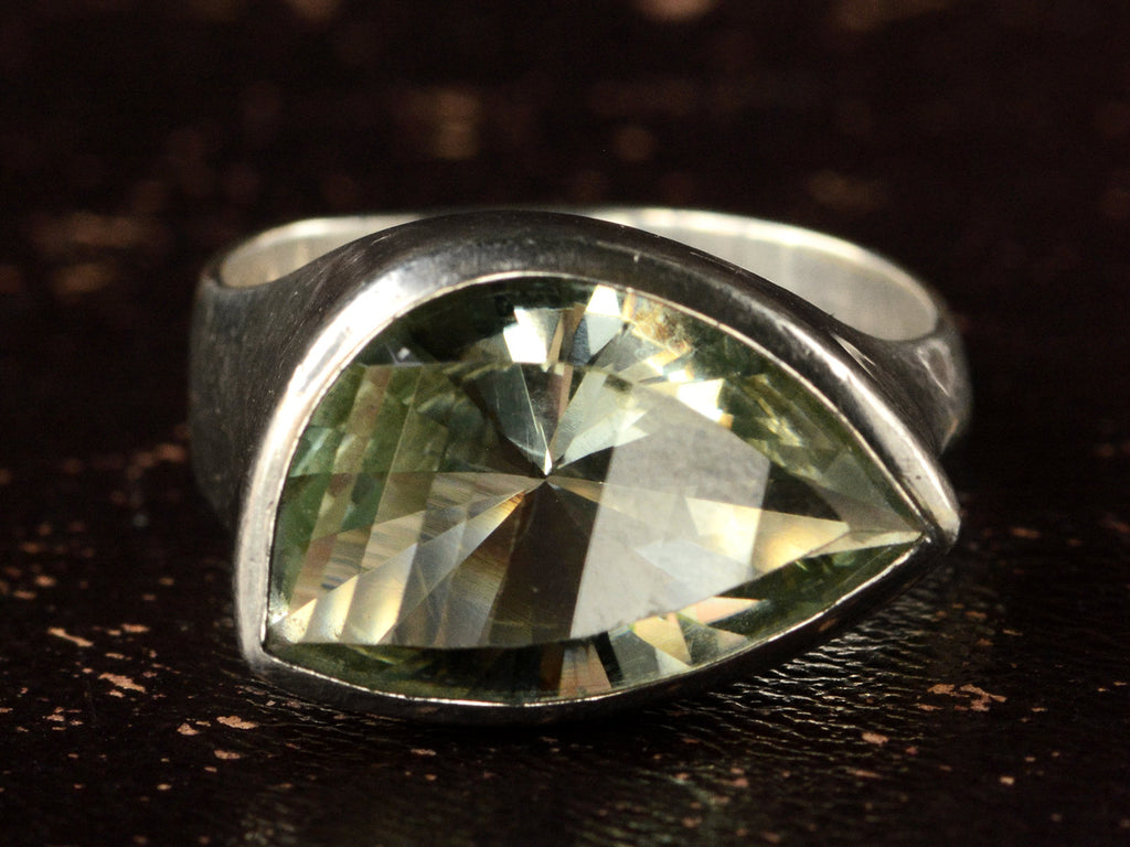 Front view of silver ring with faceted light green eye-shaped stone, shown on dark background.
