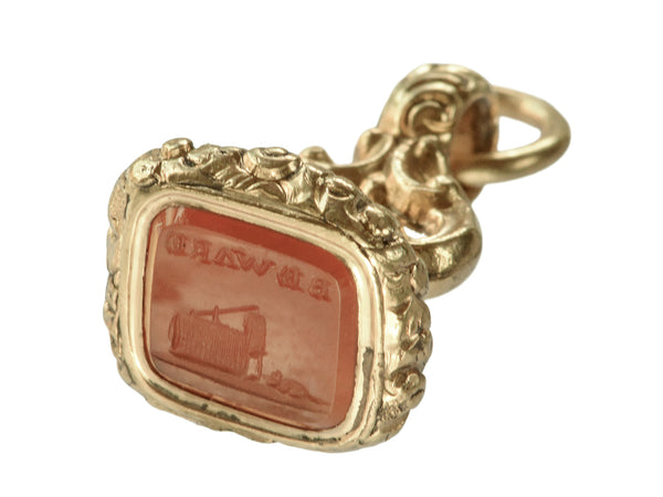 Angled view of Georgian-era gold fob with a carnelian intaglio carved with the word "BEWARE" in mirror image and the image of a mousetrap and mouse, shown on white background.