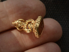 thumbnail of Angled view of Georgian-era gold fob with a carnelian intaglio carved with the word "BEWARE" in mirror image and the image of a mousetrap and mouse, shown held in hand