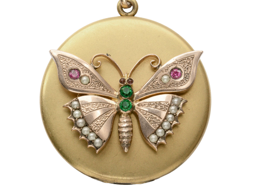 A round Victorian gilt locket with a rose gold butterfly mounted on the front, detailed with pearls and red and green paste. Shown on white background.