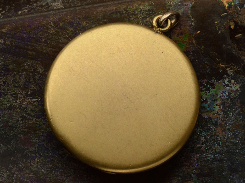 Plain reverse side of round Victorian gilt locket. Shown on dark background.