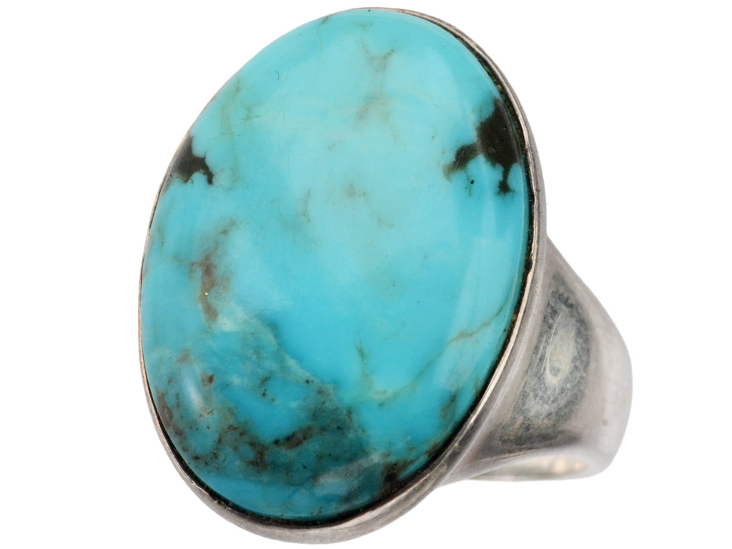 Angled view of large oval turquoise and silver ring on white background.