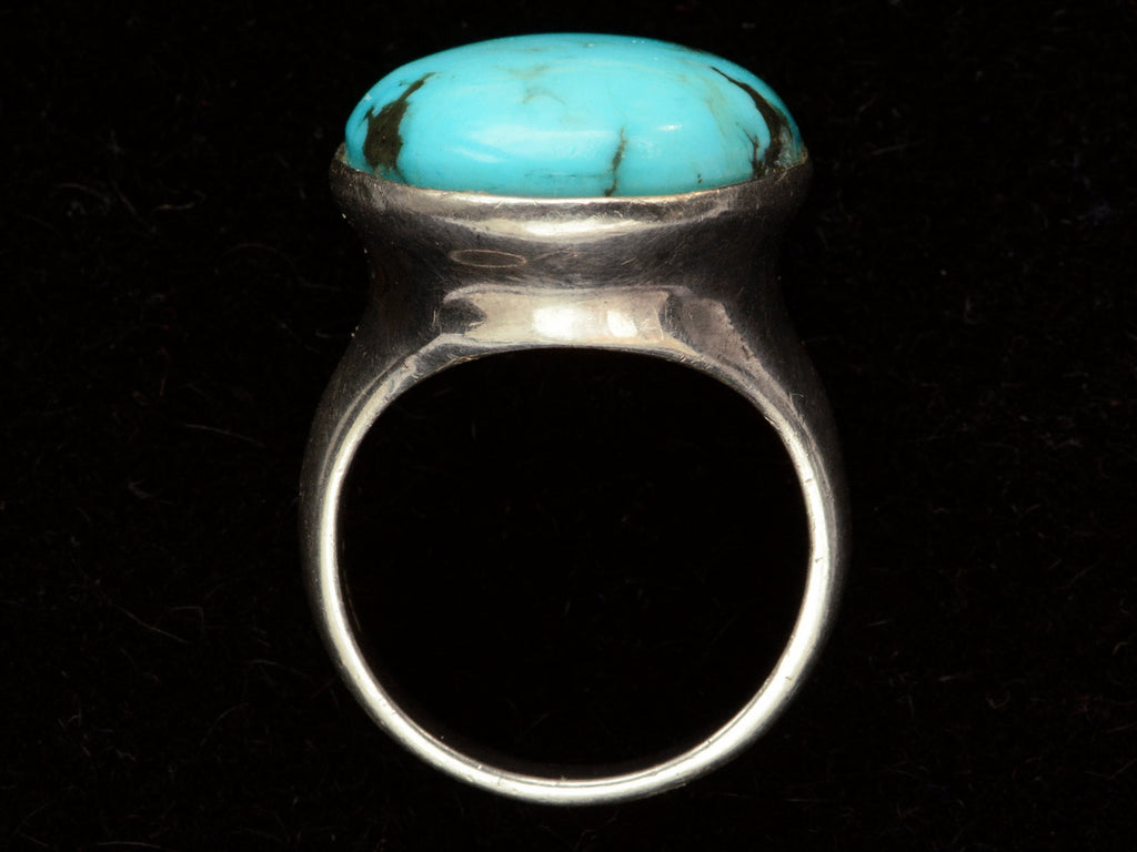 Side profile view of large oval turquoise and silver ring on black background.