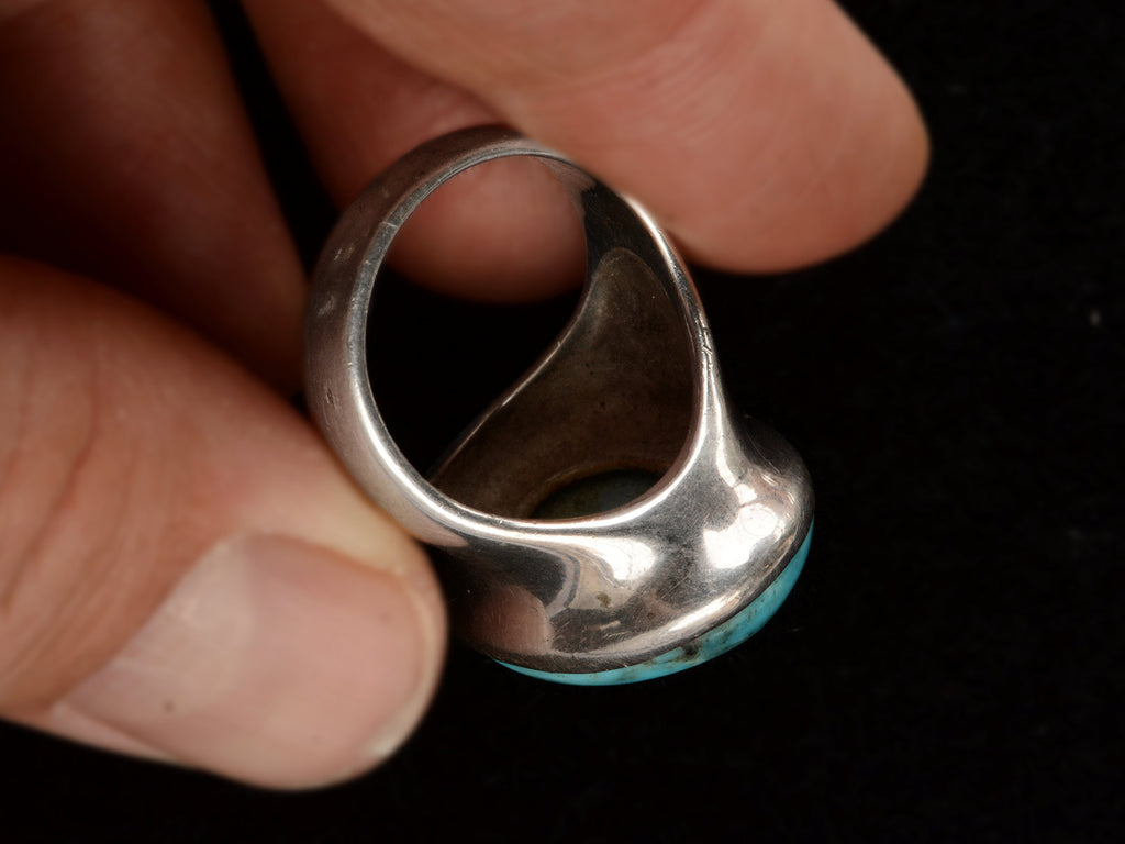 Inside view of large oval turquoise and silver ring held in hand against black background.
