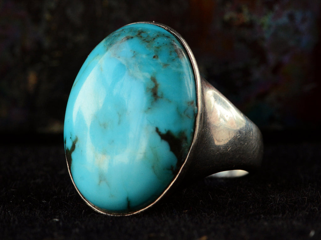 Angled view of large oval turquoise and silver ring on dark background.