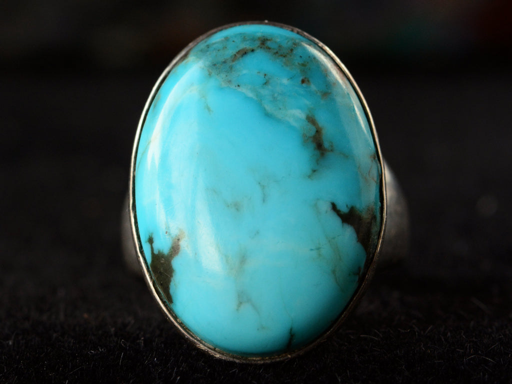 Front view of large oval turquoise and silver ring on dark background.