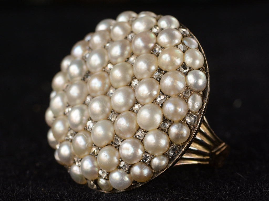 Right angled view of Victorian ring with a large luster pearls and rose cut diamonds, set in rosy-yellow gold, shown on dark background.