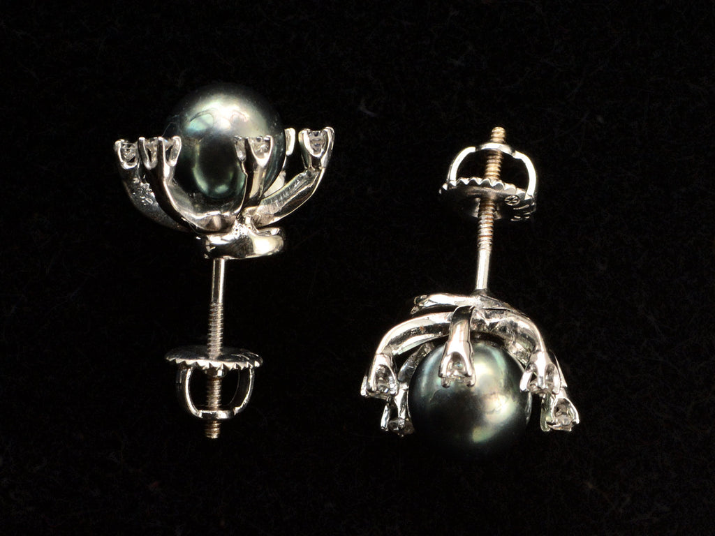 Side profile of  pair of vintage starburst stud earrings featuring a dark green-gray cultured pearls in a white gold prong setting, surrounded by six small clear diamonds on a black background.
