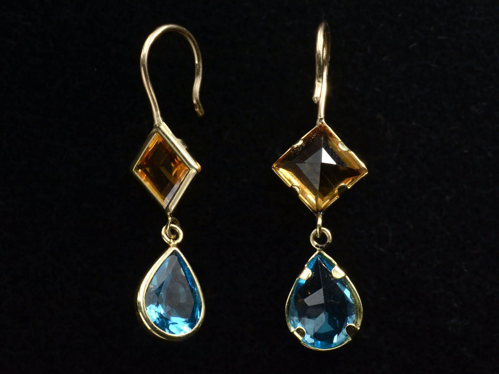 Reverse and angled views of gold earrings with diamond-shaped orange gem and teardrop-shaped blue gem on a black background