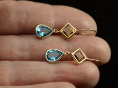 thumbnail of Gold earrings with diamond-shaped orange gem and teardrop-shaped blue gem shown on and.