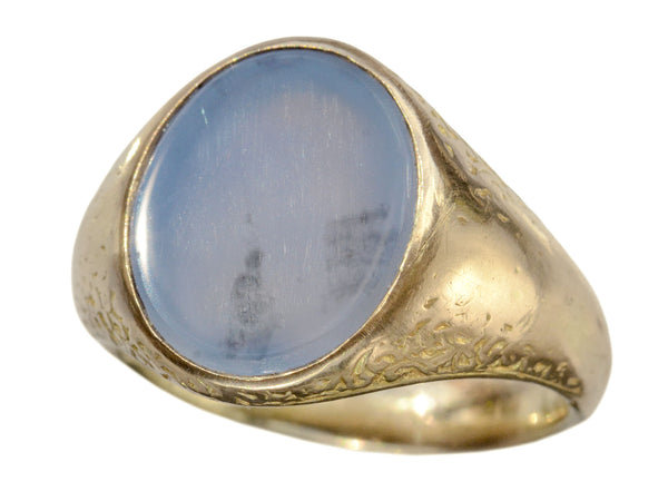 Angled view of antique gold signet ring with oval blue chalcedony face, on white background.
