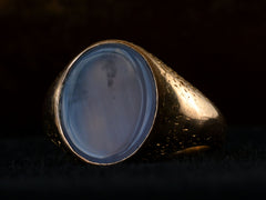thumbnail of Right angled view of antique gold signet ring with oval blue chalcedony face, on dark background.