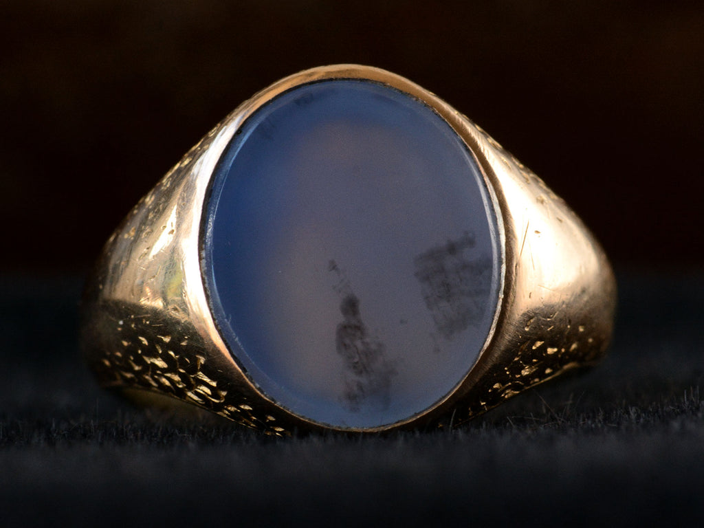 Front detail view of antique gold signet ring with oval blue chalcedony face, on dark background.