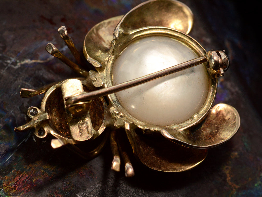 Reverse side of yellow gold insect brooch with diamond eyes and a pearl abdomen, shown on dark background. 14K stamp visible.