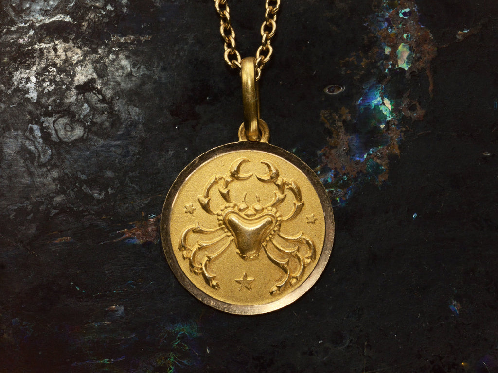 Detail of round gold pendant with a crab, shown on dark background.
