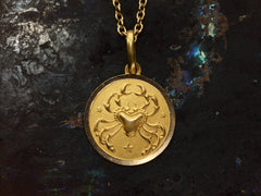 thumbnail of Detail of round gold pendant with a crab, shown on dark background.