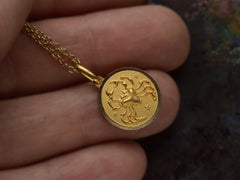 thumbnail of Round gold pendant with a crab, shown held in hand.
