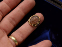 thumbnail of Front view of c1920 Art Deco ring with an oval carved blueish brown chalcedony set in a finely detailed gold mounting, shown on finger