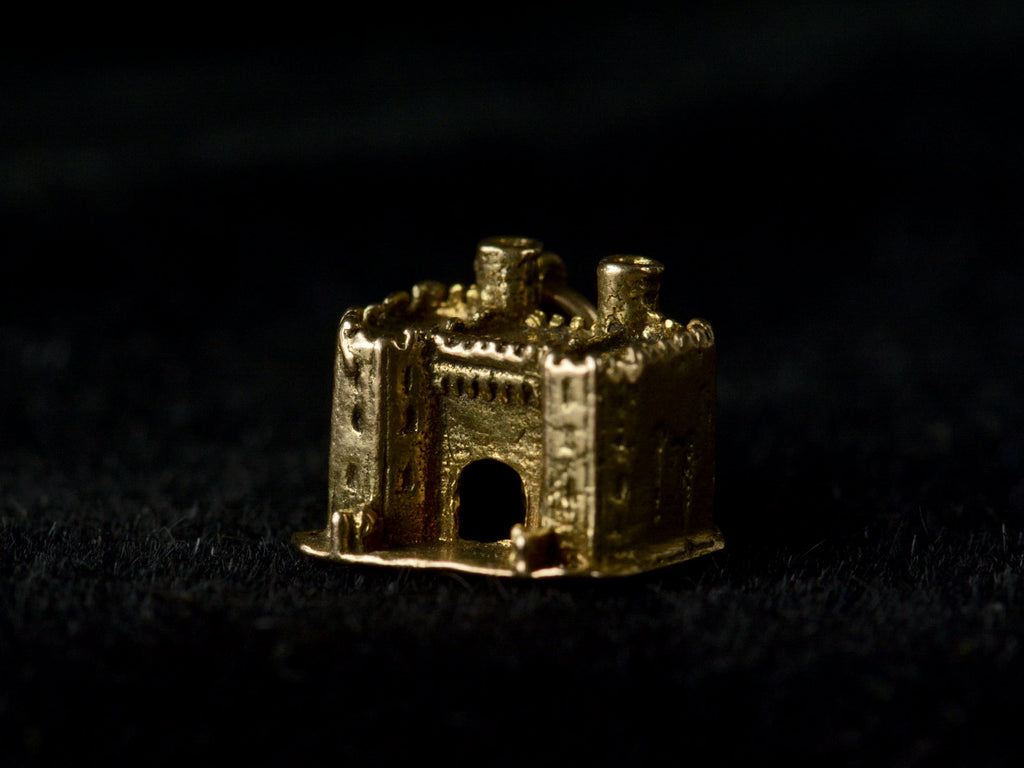 Angled view of castle charm in gold, on black background.