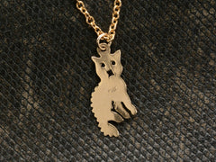 thumbnail of Reverse side of 2-dimensional yellow gold cat charm hanging on chain, shown on dark textured background. "14K" stamp visible.