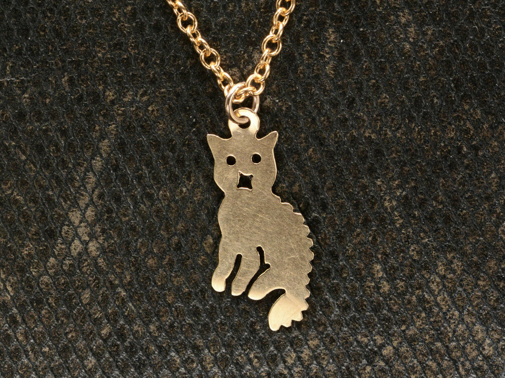 A 2-dimensional yellow gold cat charm hanging on chain, shown dark textured background.