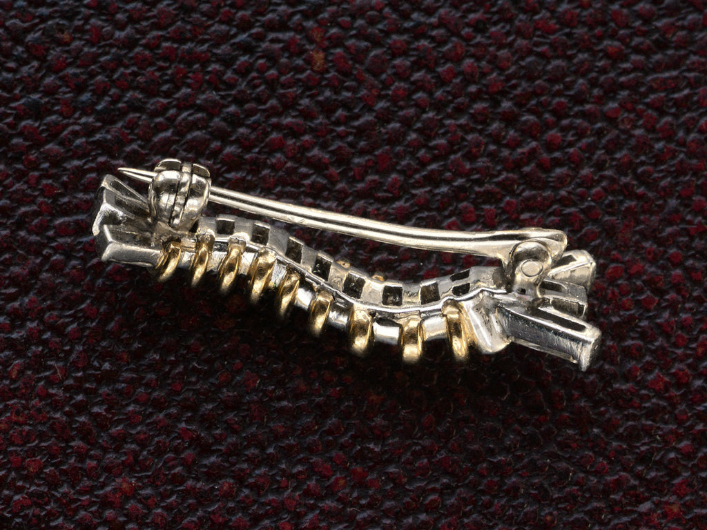 Reverse side of vintage white and yellow gold caterpillar brooch with ruby eyes and diamond baguettes, on dark textured background.