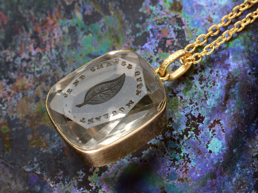 Detail of a c1820 Georgian era gold and crystal intaglio pendant carved with the image of an ivy leaf and the French phrase "Je Ne Change Qu'en Mourant." Shown colorful background.