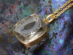 thumbnail of Detail of a c1820 Georgian era gold and crystal intaglio pendant carved with the image of an ivy leaf and the French phrase "Je Ne Change Qu'en Mourant." Shown colorful background.