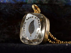 thumbnail of Angled detail view of c1820 Georgian era gold and crystal intaglio pendant carved with the image of an ivy leaf and the French phrase "Je Ne Change Qu'en Mourant." Shown on dark background.