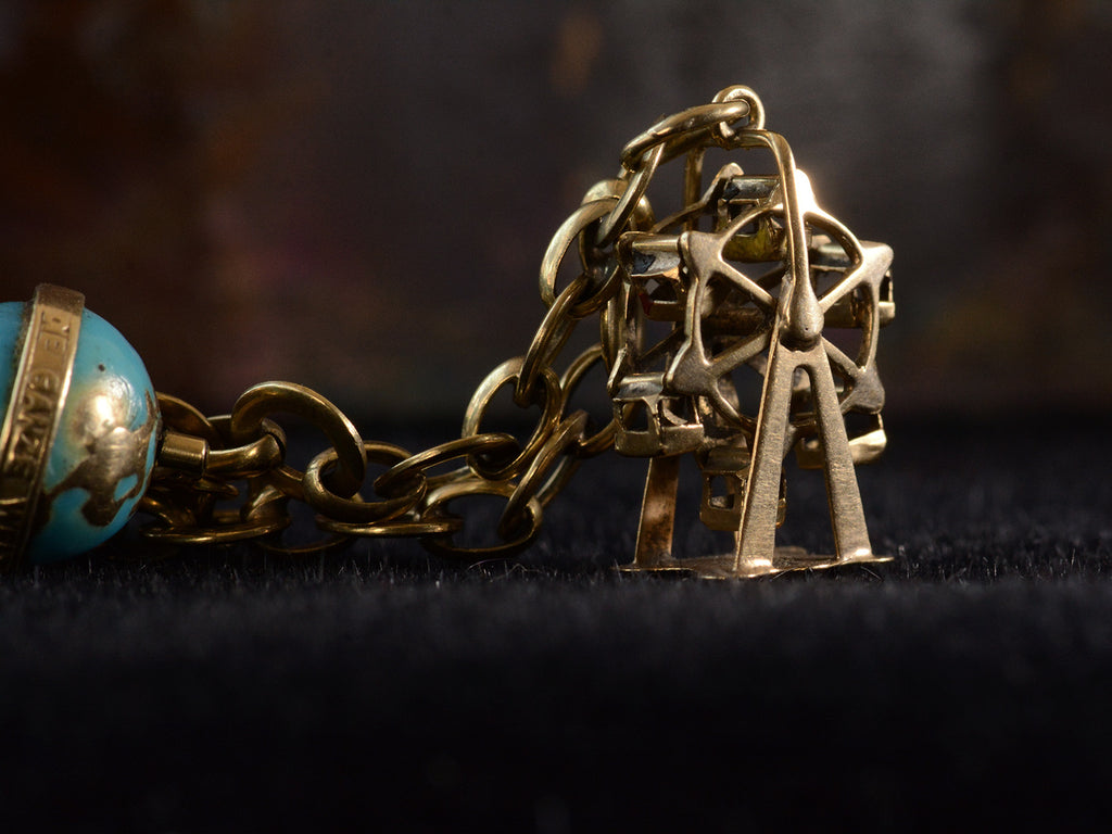 Detail view of yellow gold ferris wheel charm on dark background.