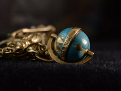 thumbnail of Detail view of yellow gold and blue enamel globe charm with the German words "UM LIEBE" visible. On dark background.