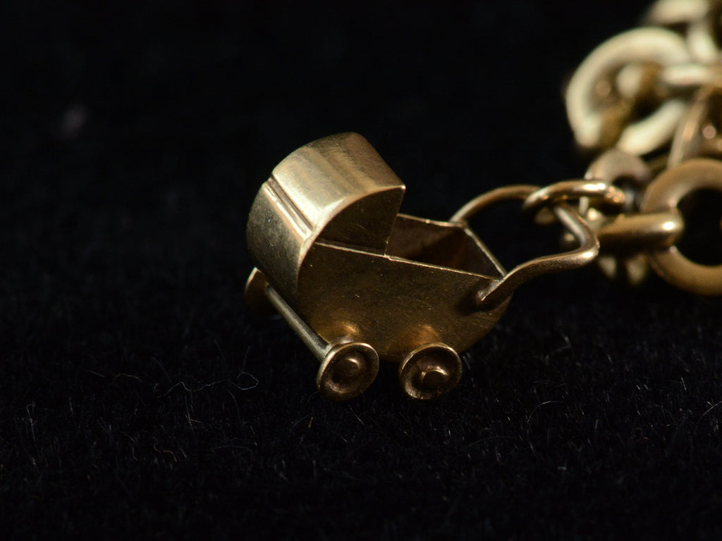 Detail view of yellow gold baby carriage charm on dark background.