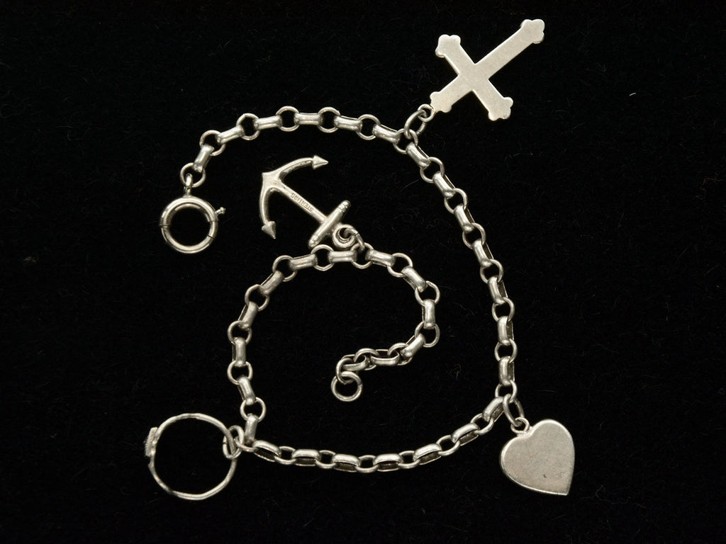 Detail view of c1930 Vintage Silver Charm Bracelet with 4 Charms: an Anchor, a Baby Ring, a Heart, and a Cross. Shown on black background.