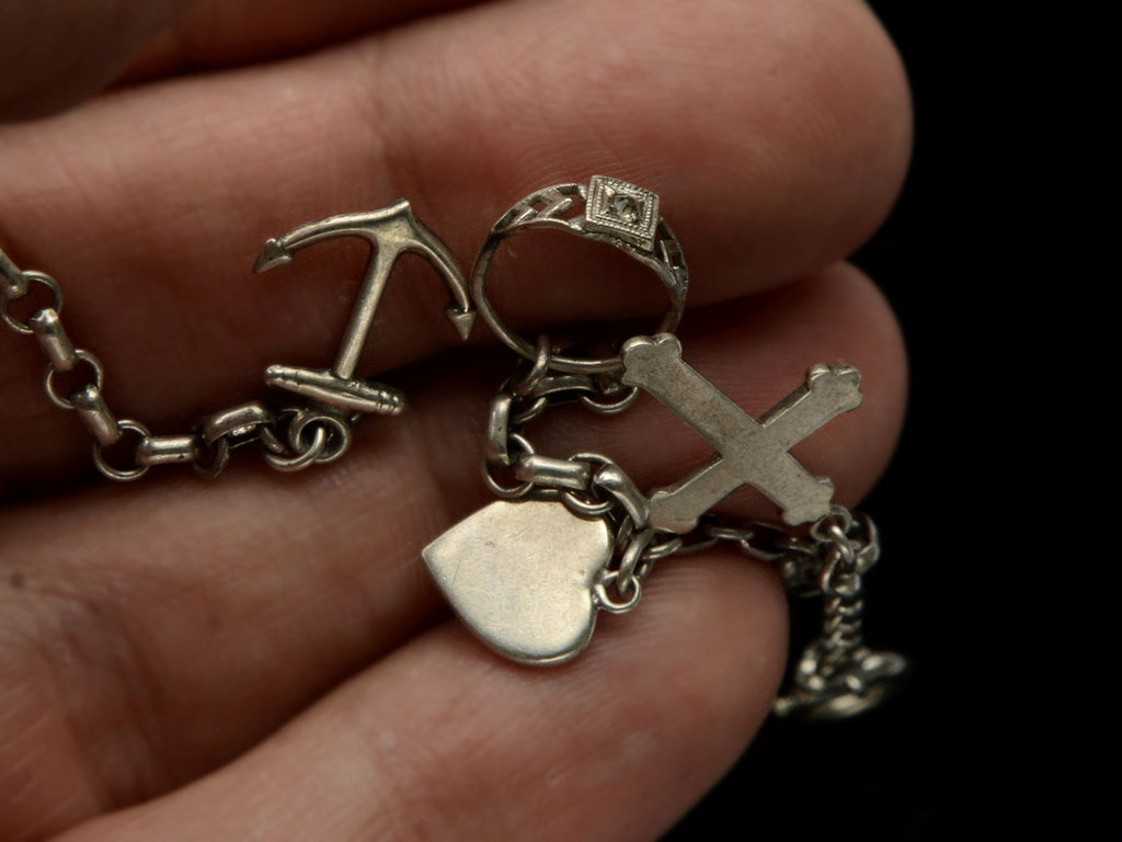 Detail view of c1930 Vintage Silver Charm Bracelet with 4 Charms: an Anchor, a Baby Ring, a Heart, and a Cross. Shown held in hand.