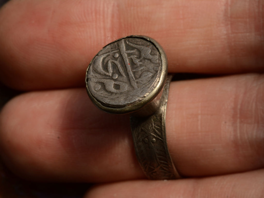Angled front view of Mughal Rupee with Arabic Lettering, mounted in silver ring. Shown on finger for scale.
