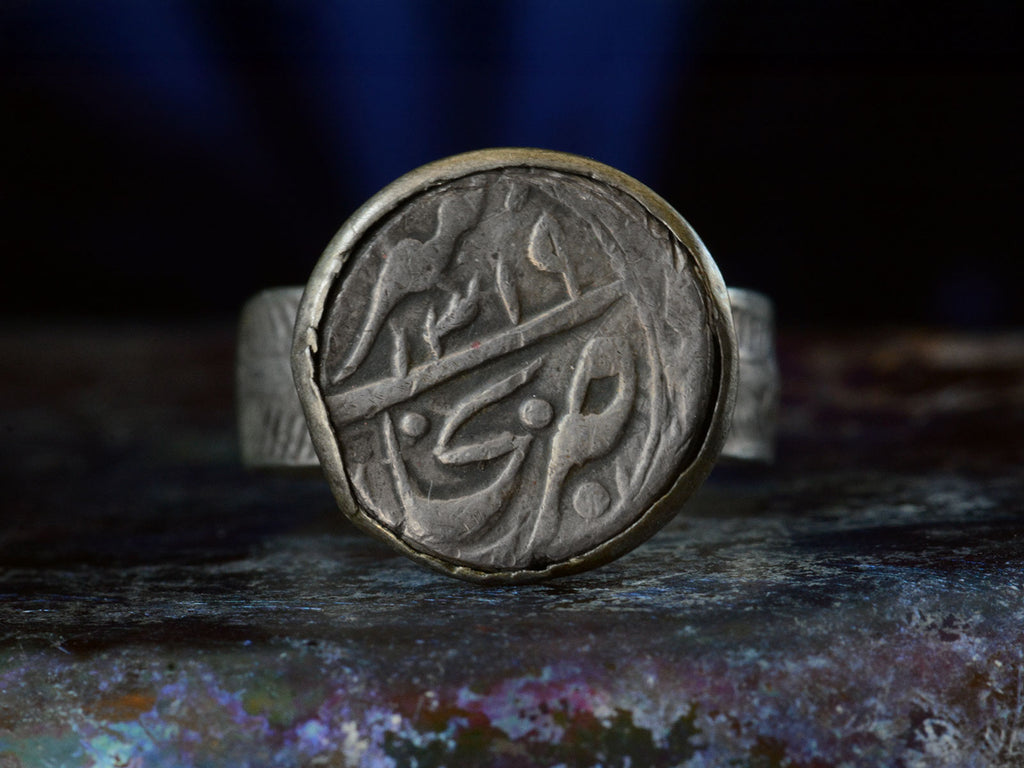 Front view of Mughal Rupee with Arabic Lettering, mounted in silver ring. Shown on dark background