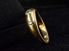 thumbnail of Side, angled view of a vintage 18k yellow gold ring flush set with a light greenish-yellow round diamond in between two smaller light pink diamonds, shown on dark background.