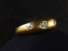 thumbnail of Angled front view of a 18k yellow gold ring flush set with a light greenish-yellow round diamond in between two smaller light pink diamonds, shown on dark background.