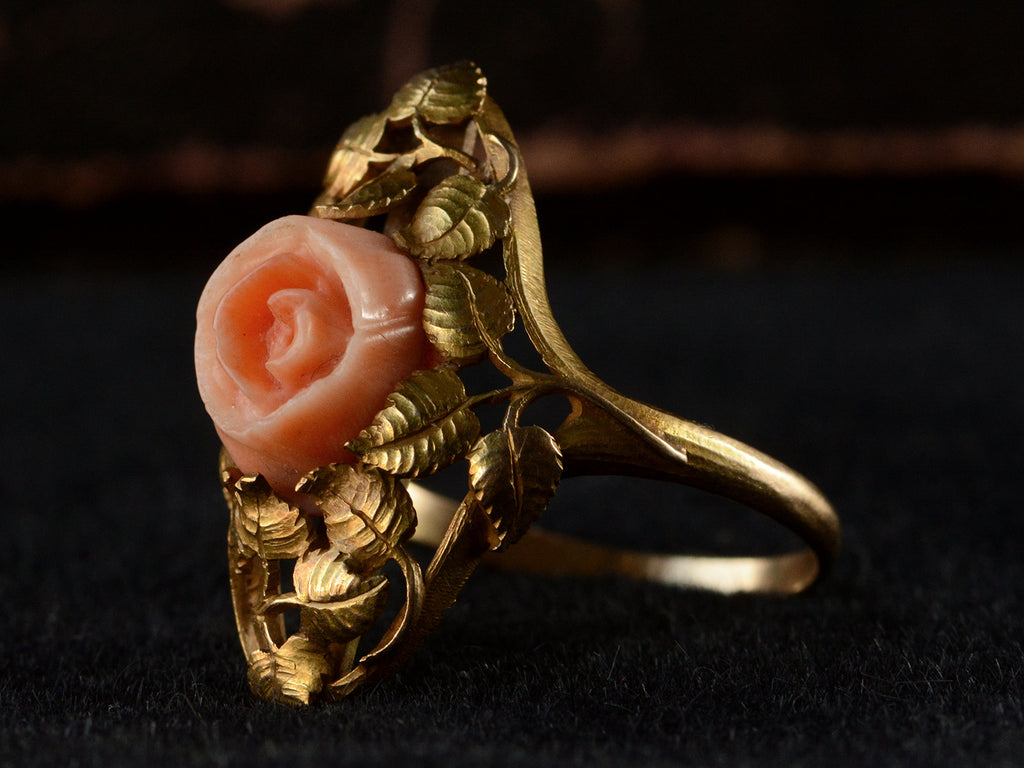 Right angled view of 1930 ring with a coral rose surrounded by gold leaves and vines, shown on black background.