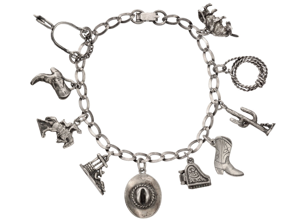 Vintage western-themed silver charm bracelet with a spur, two boots, a horse, a man sleeping in a sombrero, a cowboy hat, a piano with functioning lid, a cactus, a rope and a bull, on white background.