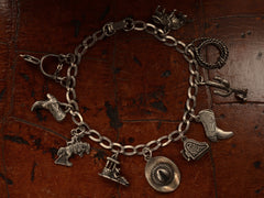 thumbnail of Vintage western-themed silver charm bracelet with a spur, two boots, a horse, a man sleeping in a sombrero, a cowboy hat, a piano with functioning lid, a cactus, a rope and a bull, on dark leather background.