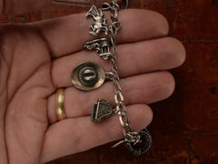 thumbnail of Detail of silver western-themed charm bracelet, held in hand.