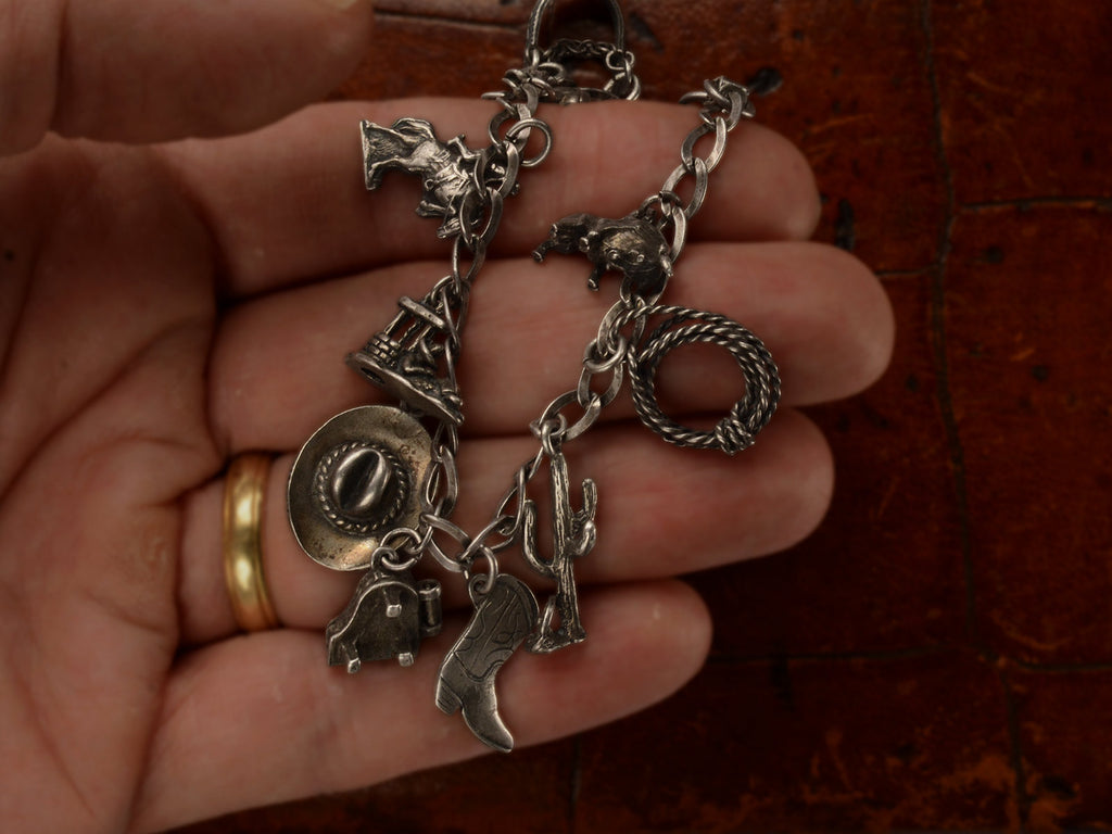 Silver western-themed charm bracelet, held in hand.