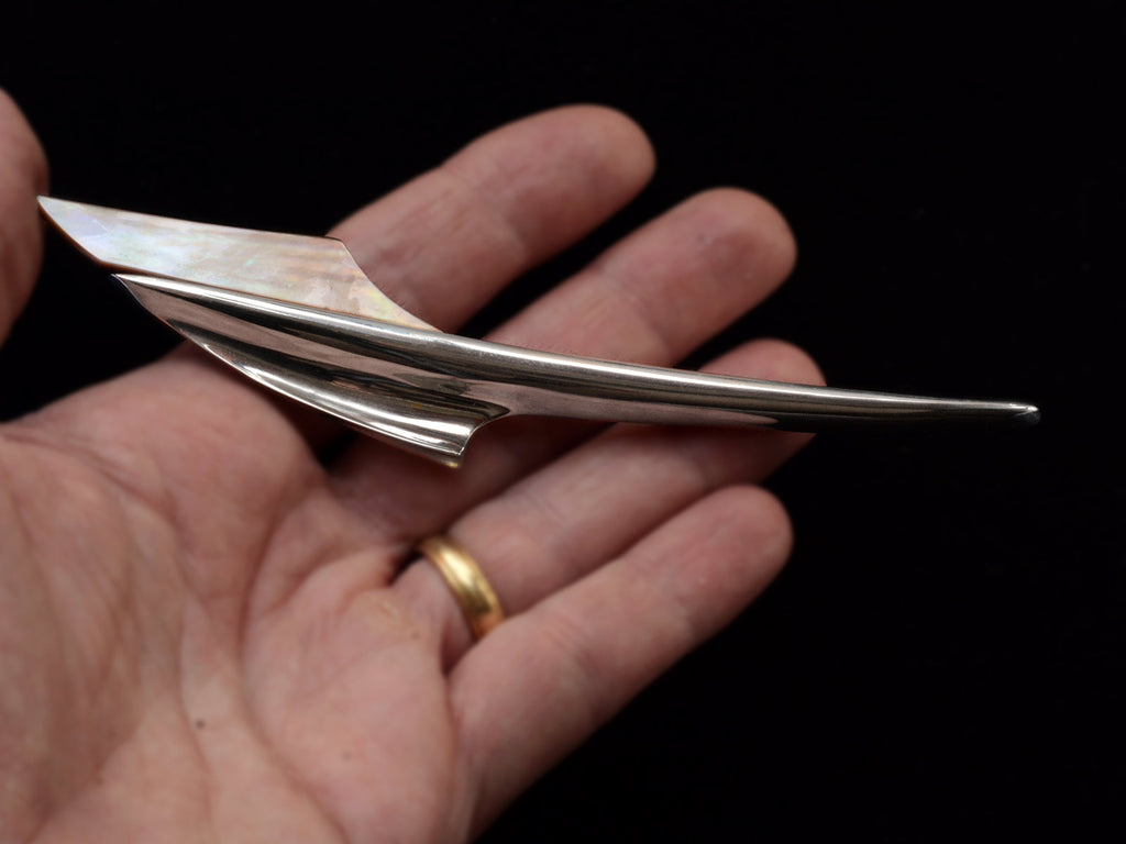Abstract rocket-ship shaped sterling and abalone brooch on hand.