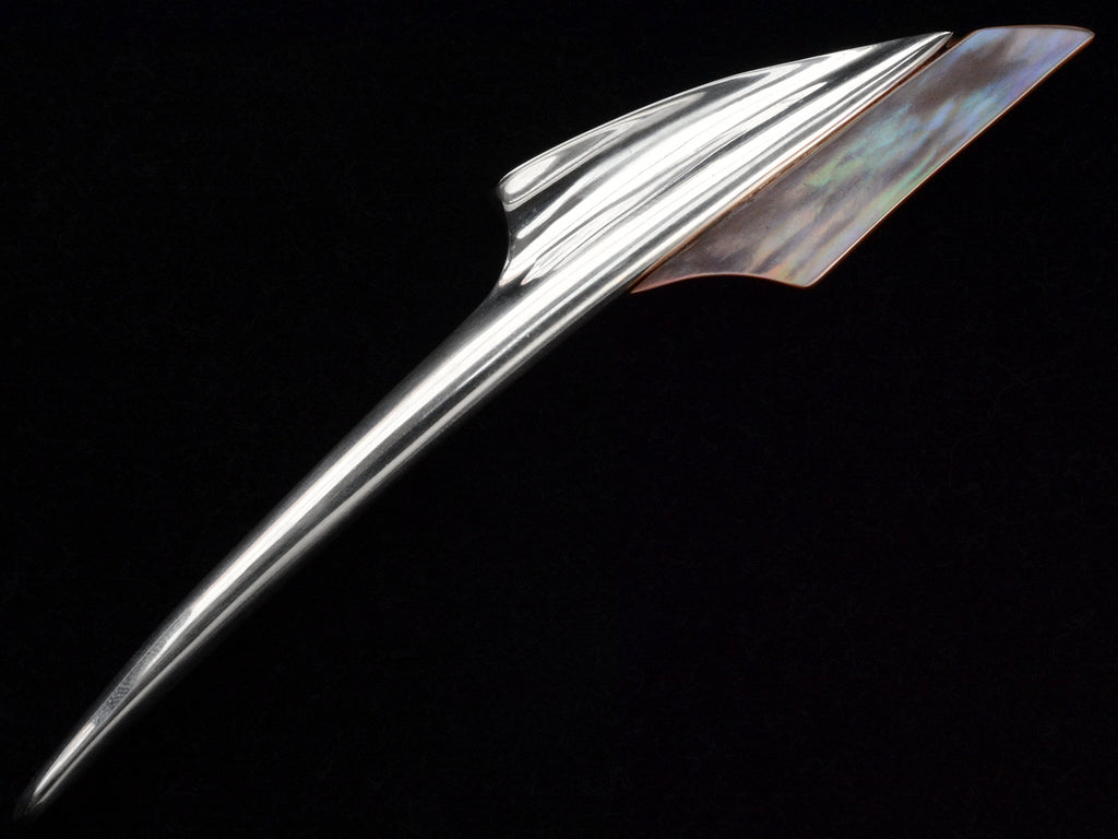 Abstract rocket-ship shaped sterling and abalone brooch on black background, showing abalone iridescence. 
