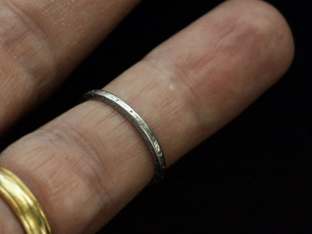 An antique platinum wedding band with engraved patterning, shown on finger for scale.