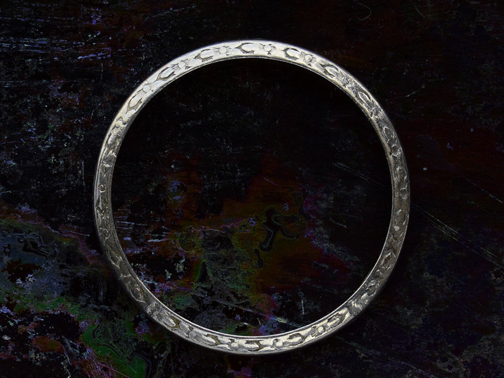 Side profile view of antique platinum wedding band with engraved patterning, shown on dark background.