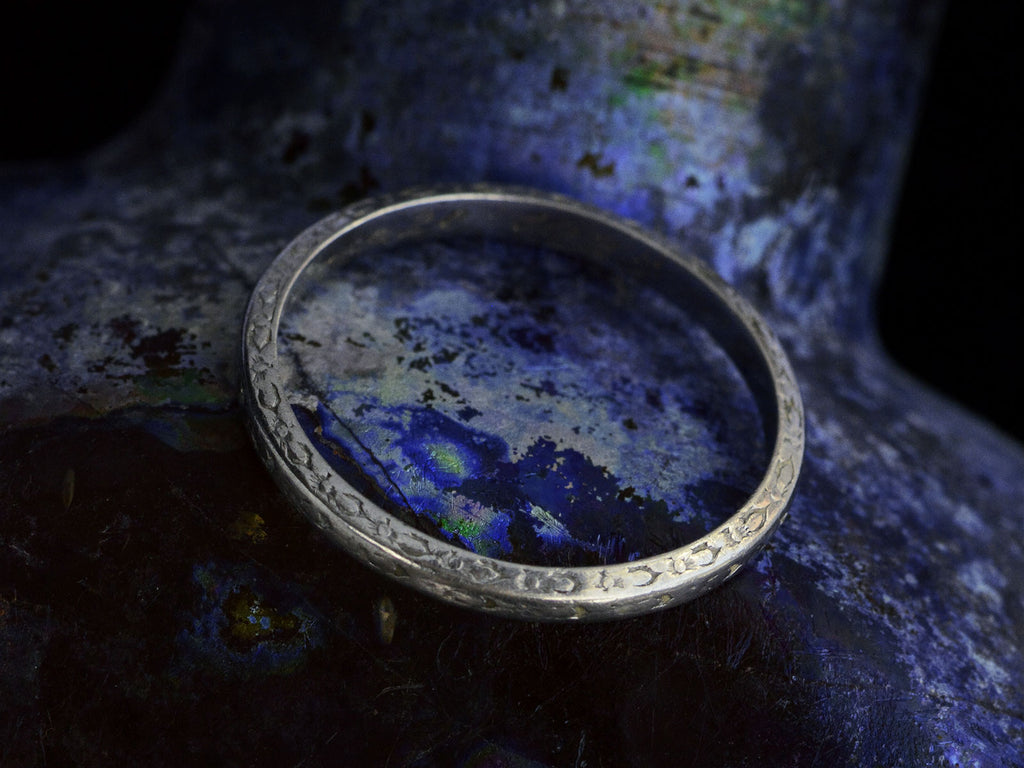 Elevated side view of antique platinum wedding band with engraved patterning, shown on dark background.