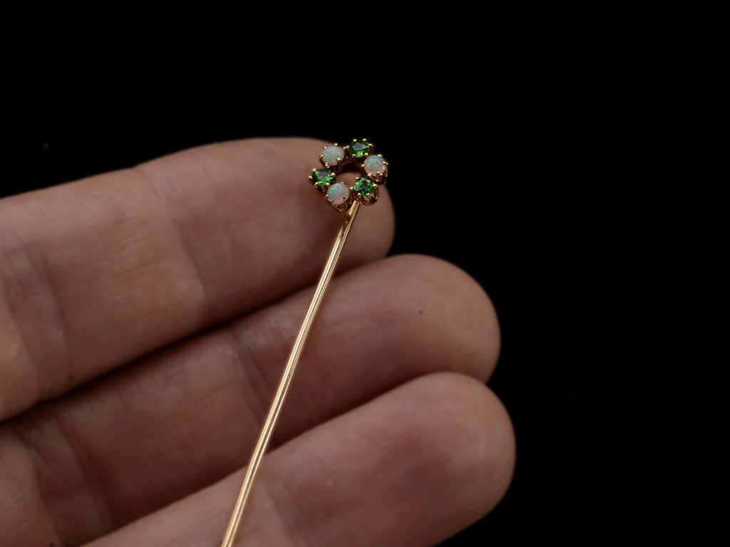 Hand holding an antique yellow gold Victorian stick pin with three opals and three vivid green demantoid garnets arranged in a circle. 