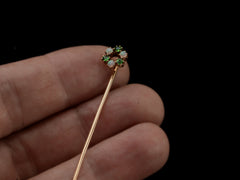 thumbnail of Hand holding an antique yellow gold Victorian stick pin with three opals and three vivid green demantoid garnets arranged in a circle. 